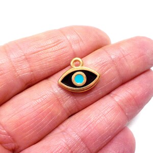 Puede incluir: Encanto de oro con un dise&ntilde;o de ojo turco negro y azul. El encanto es un s&iacute;mbolo popular de protecci&oacute;n y buena suerte.