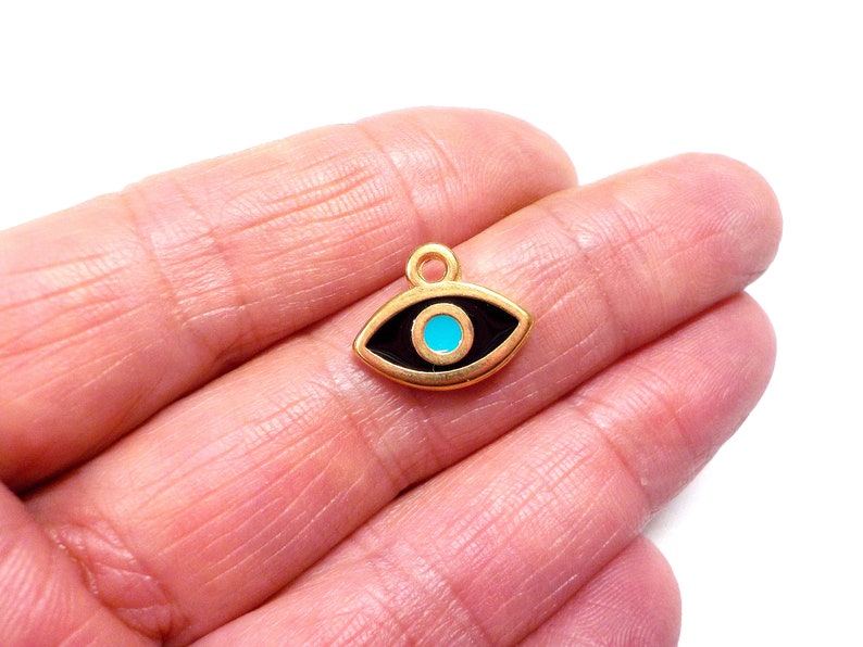 Puede incluir: Encanto de oro con un dise&ntilde;o de ojo turco negro y azul. El encanto es un s&iacute;mbolo popular de protecci&oacute;n y buena suerte.