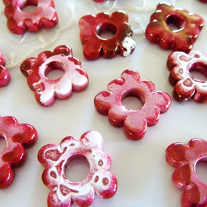 Puede incluir: Una colecci&oacute;n de cuentas de cer&aacute;mica de color rojo y blanco con forma de flor y un agujero en el centro. Las cuentas tienen un acabado brillante y son perfectas para hacer joyas o manualidades.