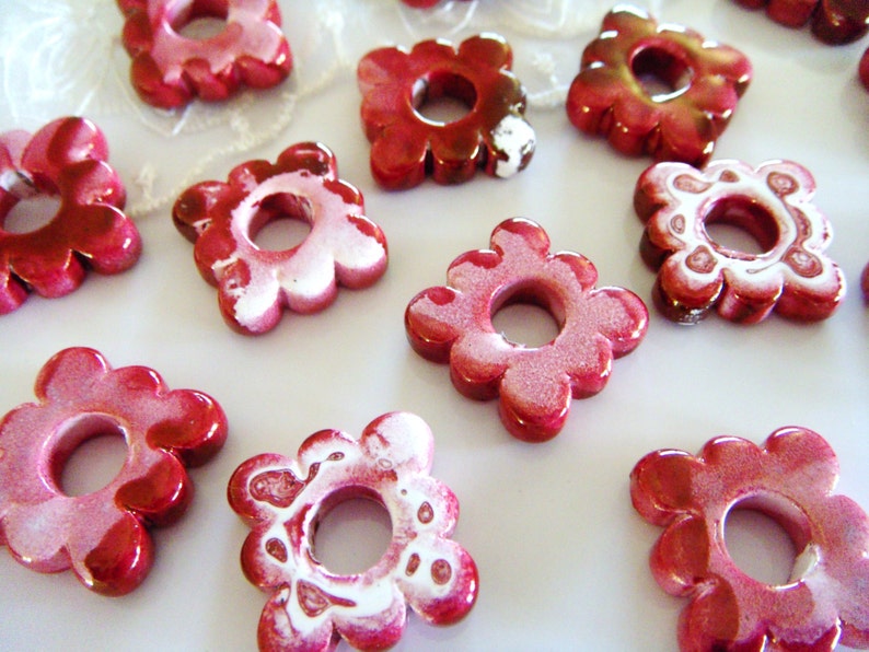 Puede incluir: Una colecci&oacute;n de cuentas de cer&aacute;mica de color rojo y blanco con forma de flor y un agujero en el centro. Las cuentas tienen un acabado brillante y son perfectas para hacer joyas o manualidades.
