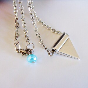 May include: A silver chain necklace with a silver triangle pendant and a light blue crystal bead.