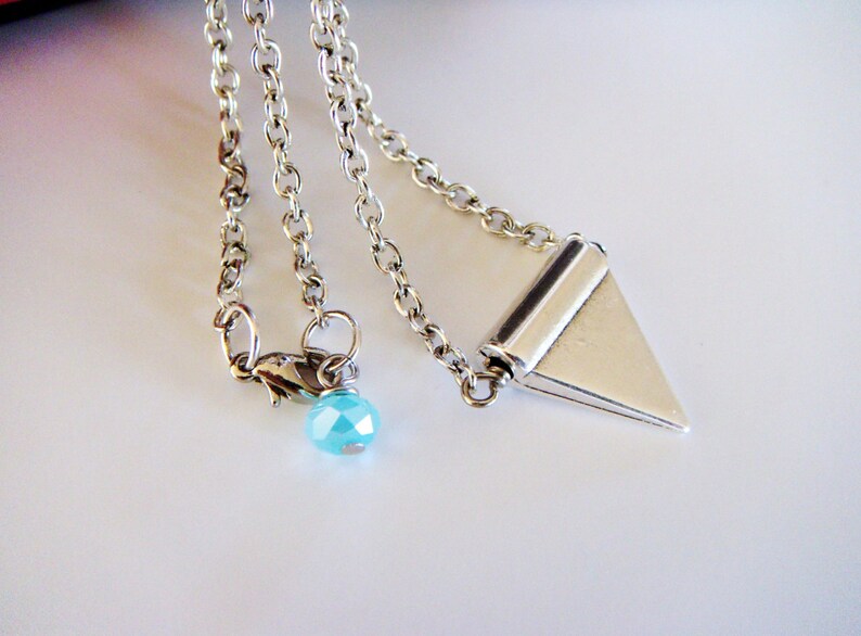 May include: A silver chain necklace with a silver triangle pendant and a light blue crystal bead.