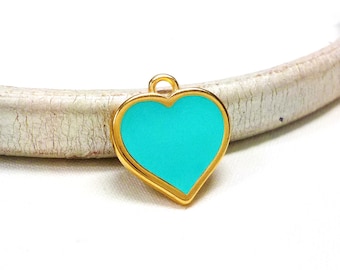 Puede incluir: Un colgante de corazón de color dorado con un relleno de esmalte azul turquesa. El colgante tiene un bucle en la parte superior para sujetarlo a una cadena o cordón.