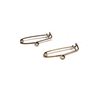 Puede incluir: Dos imperdibles de color dorado, cada uno con un diseño sencillo y una cabeza redonda.