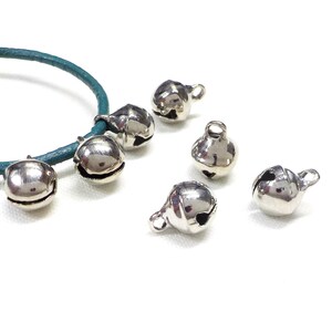 May include: Silver jingle bells with a teal cord. The bells are small and have a rounded shape with a hole at the top for threading.