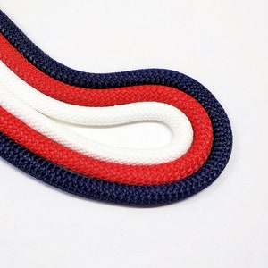 May include: Three strands of rope, one navy blue, one red, and one white, are braided together in a circular shape.