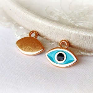 Puede incluir: Dos abalorios de metal dorado en forma de ojo. Un abalorio es una forma de ojo s&oacute;lida, mientras que el otro abalorio tiene un ojo de esmalte azul y blanco con una pupila negra.
