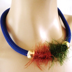 May include: A blue crocheted necklace with a gold bead and a red and green fuzzy accent.