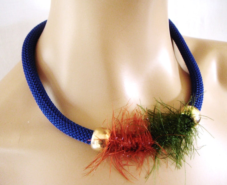 May include: A blue crocheted necklace with a gold bead and a red and green fuzzy accent.