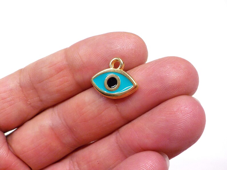 May include: Gold-tone charm with a blue evil eye design. The charm has a black pupil and a gold loop for attaching to a necklace or bracelet.