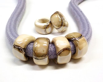 Könnte beinhalten: Nahaufnahme einer Halskette mit fünf beige-braunen Perlen. Die Perlen sind aus einem Material, das wie Marmor aussieht. Die Halskette besteht aus einem hellvioletten Band.
