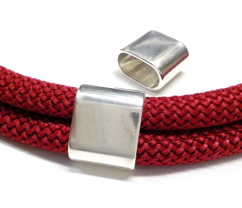 May include: Two silver metal cord end caps for a red rope or cord. The cord end caps are rectangular in shape and have a smooth, polished finish.