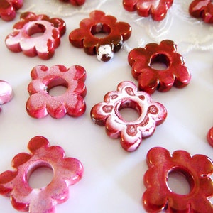 Puede incluir: Una colecci&oacute;n de cuentas de cer&aacute;mica de color rojo y blanco con forma de flor y un agujero en el centro. Las cuentas tienen un acabado brillante y son perfectas para hacer joyas o manualidades.