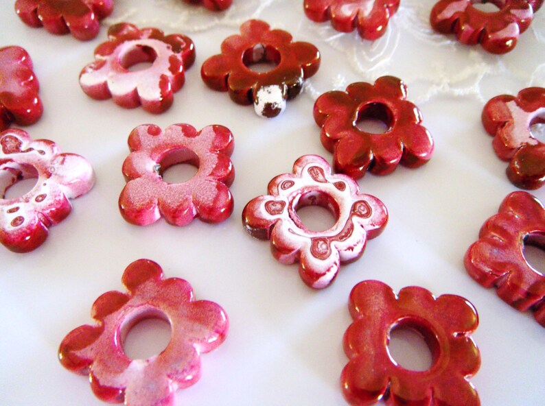 Puede incluir: Una colecci&oacute;n de cuentas de cer&aacute;mica de color rojo y blanco con forma de flor y un agujero en el centro. Las cuentas tienen un acabado brillante y son perfectas para hacer joyas o manualidades.