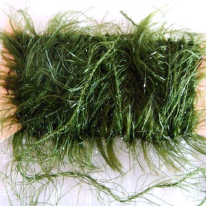 May include: A spool of green sparkly yarn with a fuzzy texture. The yarn is wrapped around a cardboard spool.