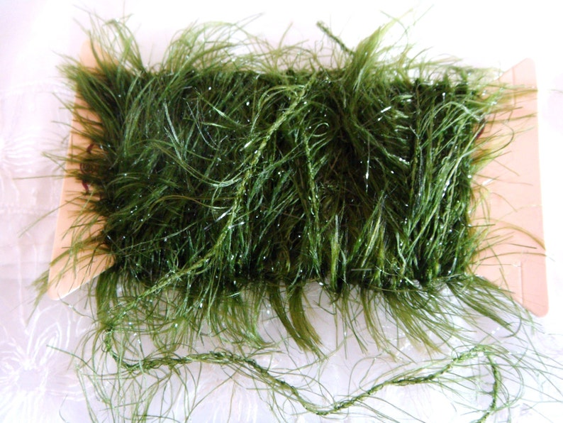 May include: A spool of green sparkly yarn with a fuzzy texture. The yarn is wrapped around a cardboard spool.