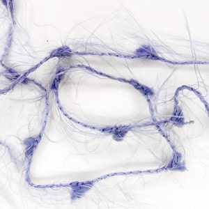 May include: Close-up of a tangled, light purple yarn with a fuzzy texture. The yarn is composed of thin, transparent strands and thicker, knotted sections of a darker purple color. The background is plain white, highlighting the yarn's intricate details.