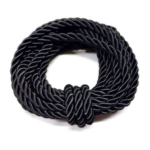 May include: A black braided rope is coiled into a circle, with the ends tied together in a knot.
