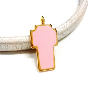 May include: Gold-toned cross charm with a pink enamel fill. The charm has a loop at the top for attaching to a necklace or bracelet.