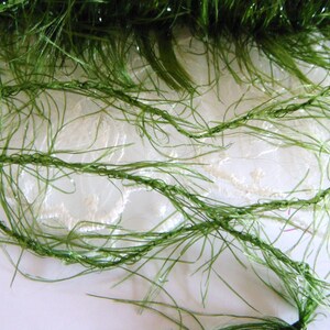 May include: Green fuzzy yarn with a sparkly finish. The yarn is on a white lace background.