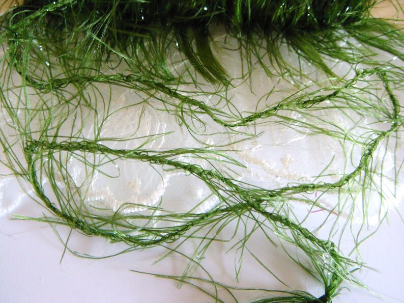 May include: Green fuzzy yarn with a sparkly finish. The yarn is on a white lace background.