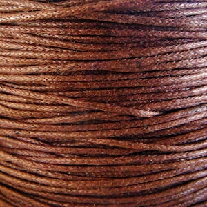 May include: Close-up of a spool of brown waxed cotton cord. The cord is tightly wound and has a smooth, polished finish.
