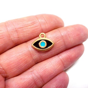 Puede incluir: Encanto dorado con un ojo de esmalte negro y un centro azul turquesa. El encanto tiene forma de ojo y tiene un bucle en la parte superior para sujetarlo a un collar o pulsera.