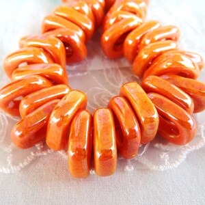 Puede incluir: Una hebra de cuentas de cer&aacute;mica de color naranja brillante, cada cuenta tiene la forma de un rect&aacute;ngulo ligeramente curvado. Las cuentas est&aacute;n dispuestas en espiral, creando un dise&ntilde;o &uacute;nico y visualmente atractivo.