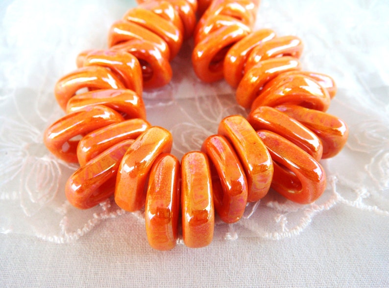 Puede incluir: Una hebra de cuentas de cer&aacute;mica de color naranja brillante, cada cuenta tiene la forma de un rect&aacute;ngulo ligeramente curvado. Las cuentas est&aacute;n dispuestas en espiral, creando un dise&ntilde;o &uacute;nico y visualmente atractivo.