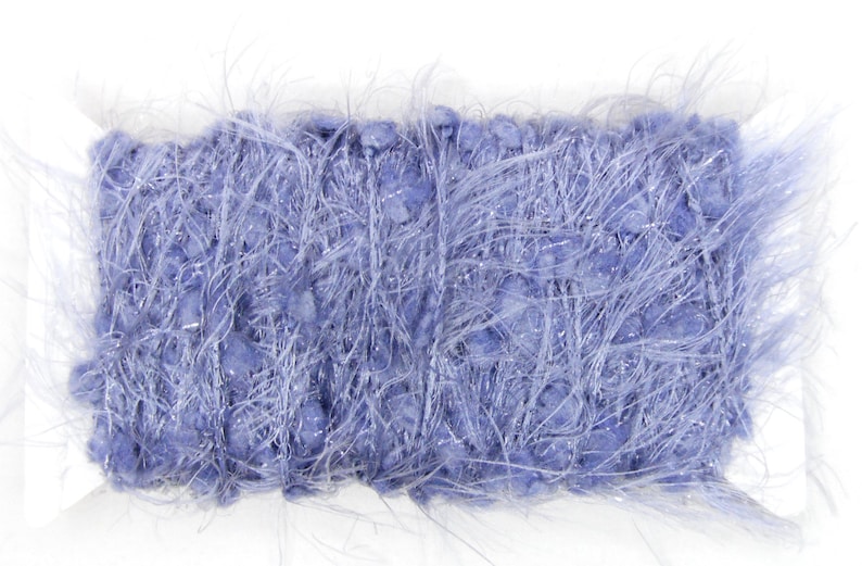 May include: A rectangular skein of blue yarn with a fluffy, textured appearance. The yarn has a soft, fuzzy texture with strands of silver thread woven throughout, creating a shimmering effect. Ideal for knitting and crochet projects.