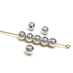 May include: Silver beads with an eye design. The beads are strung on a gold wire.
