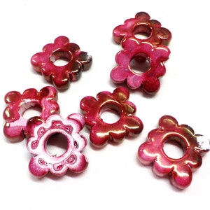 Puede incluir: Siete cuentas de color rosa y blanco con forma de flor y un agujero en el centro. Las cuentas tienen un acabado brillante.