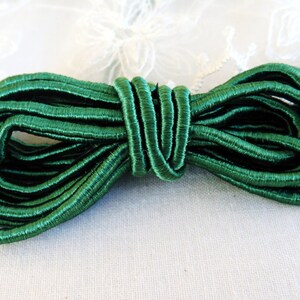May include: A spool of dark green elastic cord. The cord is tightly wound and has a satin-like finish.