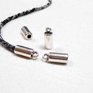 May include: Four silver metal cord end caps. Two of the caps have a loop on the end. The caps are on a white surface.