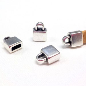 Könnte beinhalten: Quadratische Endkappen aus silberfarbenem Metall mit Schlaufe und ein Korken. Die Endkappen sind klein, rechteckig und haben eine Schlaufe zum Befestigen an einer Schnur. Der Korken ist hellbraun.