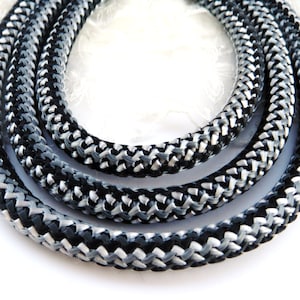 Może przedstawiać: Zbliżenie na pleciony sznur w kolorze czarnym i srebrnym. Sznur wykonany jest z dwóch różnych rodzajów sznurka, jednego czarnego i jednego srebrnego, które są splecione ze sobą, tworząc unikowy wzór.