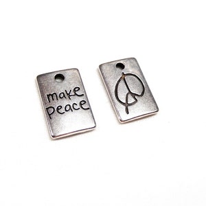 Può includere: Due ciondoli in argento con un segno di pace e le parole "make peace" su di essi.
