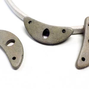 May include: Three gray ceramic crescent moon shapes with holes. Each moon has two small holes on the curved edge and one larger hole in the center.