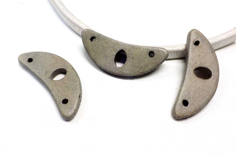 May include: Three gray ceramic crescent moon shapes with holes. Each moon has two small holes on the curved edge and one larger hole in the center.