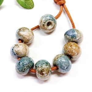 Puede incluir: Una cadena de cuentas de cerámica con un esmalte moteado azul, verde y marrón. Las cuentas están enhebradas en un cordón marrón.