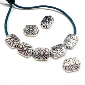 May include: Silver tone metal beads with a decorative design. The beads are strung on a teal leather cord.