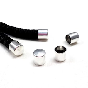 Puede incluir: Cinco terminales de cordón de metal plateado para usar con cuerda o cordón. Los terminales de cordón son cilíndricos y tienen un acabado liso.