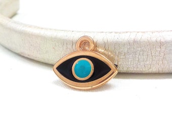 Puede incluir: Colgante en forma de ojo de color dorado, con un contorno de esmalte negro y un centro azul turquesa. El colgante tiene un pequeño lazo en la parte superior para colgarlo. El amuleto de ojo es un símbolo de protección popular.