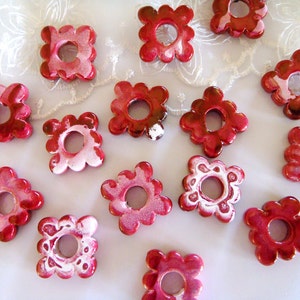 Puede incluir: Una colecci&oacute;n de 14 botones de cer&aacute;mica de forma floral, de color rojo y blanco, con un agujero en el centro. Los botones tienen un borde festoneado y un dise&ntilde;o de espiral blanco.