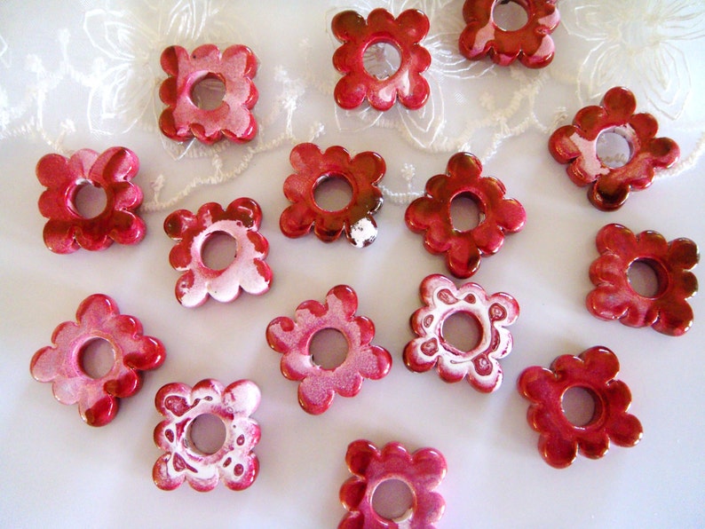 Puede incluir: Una colecci&oacute;n de 14 botones de cer&aacute;mica de forma floral, de color rojo y blanco, con un agujero en el centro. Los botones tienen un borde festoneado y un dise&ntilde;o de espiral blanco.
