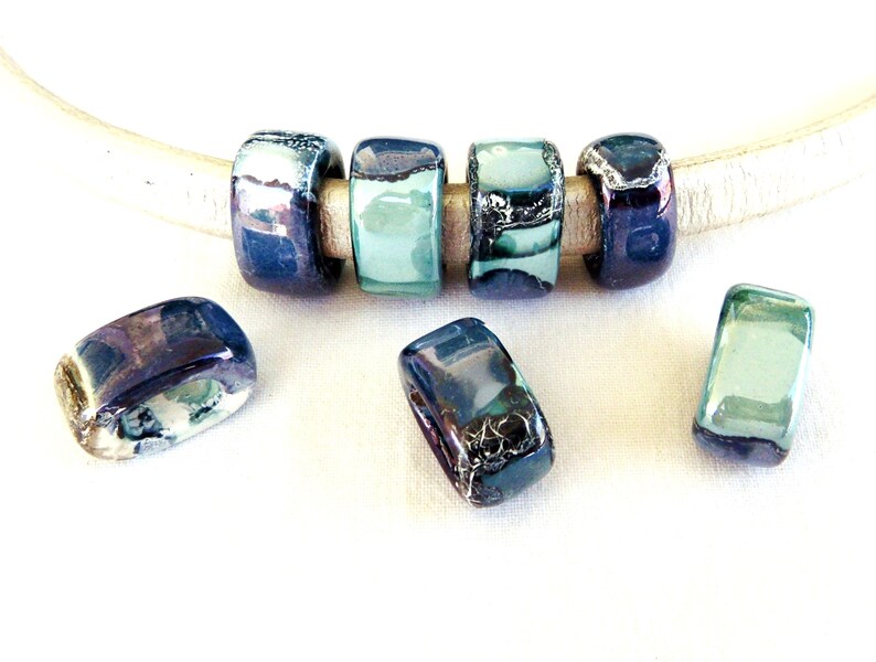 May include: A set of six rectangular ceramic beads with a blue, green, and silver glaze. The beads are strung on a white leather cord.
