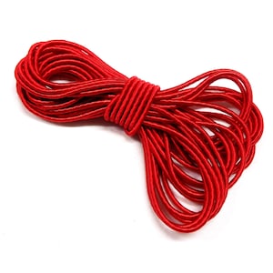 Può includere: Un fascio di cordoncino elastico rosso brillante, strettamente avvolto e ad anello. Il cordoncino appare liscio e lucido. Lo sfondo è bianco, evidenziando il colore vibrante e la consistenza dell'elastico.