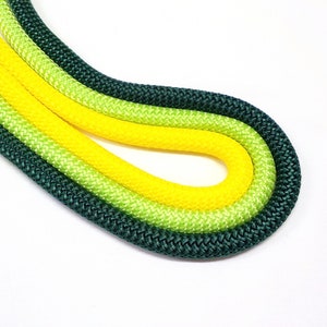 May include: Three ropes of different colours, green, light green, and yellow, are twisted together. The ropes are made of a braided material.