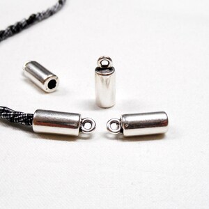 May include: Four silver metal cord end caps, two with loops and two without. The cord end caps are designed to be used with cord or string.