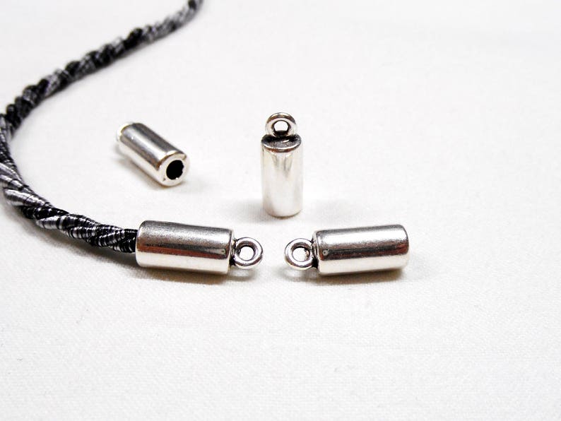 May include: Four silver metal cord end caps, two with loops and two without. The cord end caps are designed to be used with cord or string.